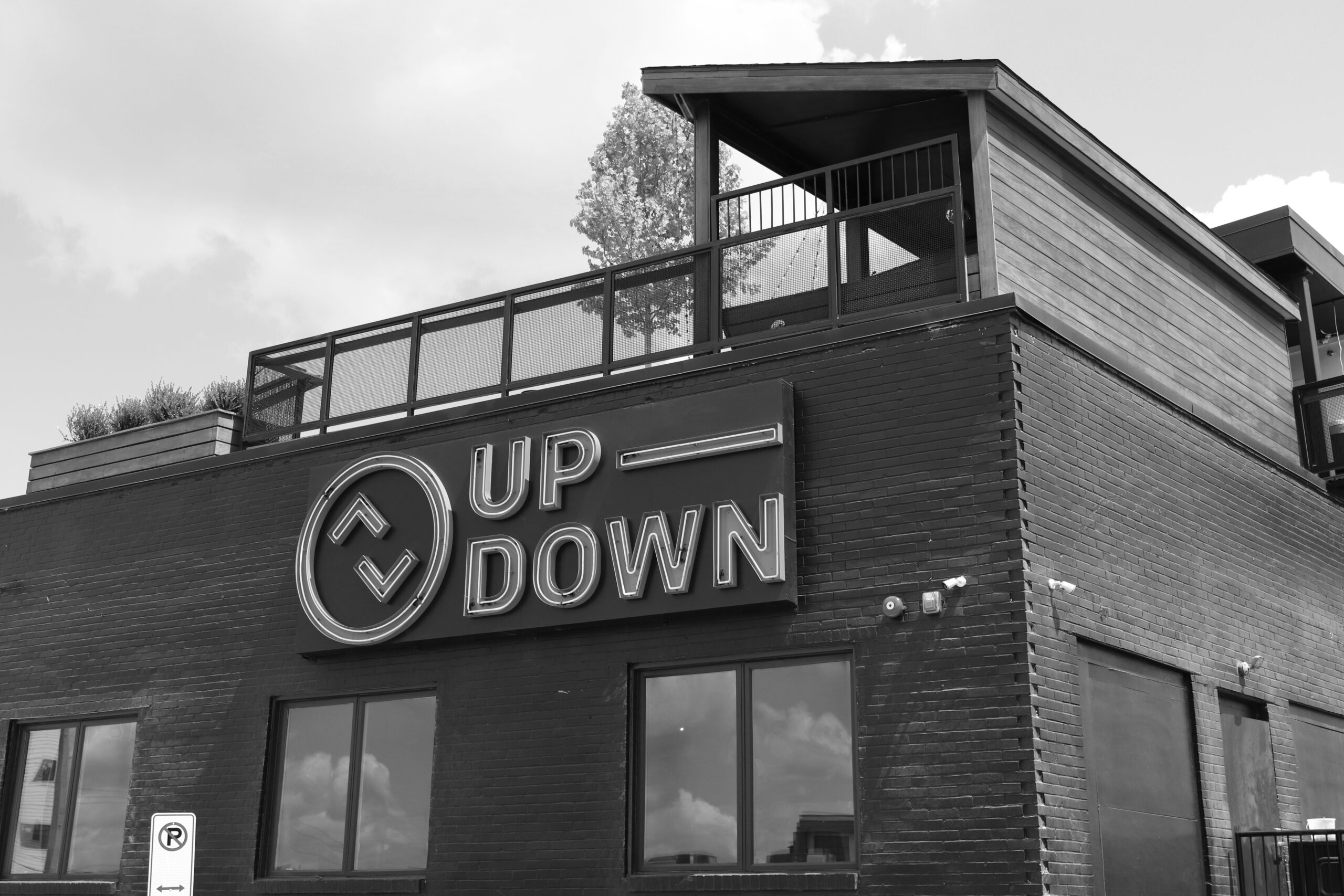 A greyscale, low-angle shot of the Up-Down bar, showcasing its black brick exterior and neon sign.