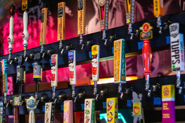 A close-up shot of several beer taps lined up in a row, with colorful handles and various brand logos A close-up shot of several beer taps lined up in a row, with colorful handles and various brand logos