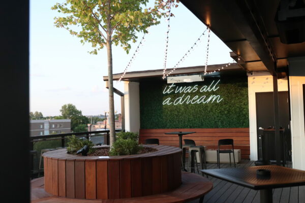 A panoramic view of the rooftop bar's patio area, featuring tables, chairs, and city skyline in the background A panoramic view of the rooftop bar's patio area, featuring tables, chairs, and city skyline in the background