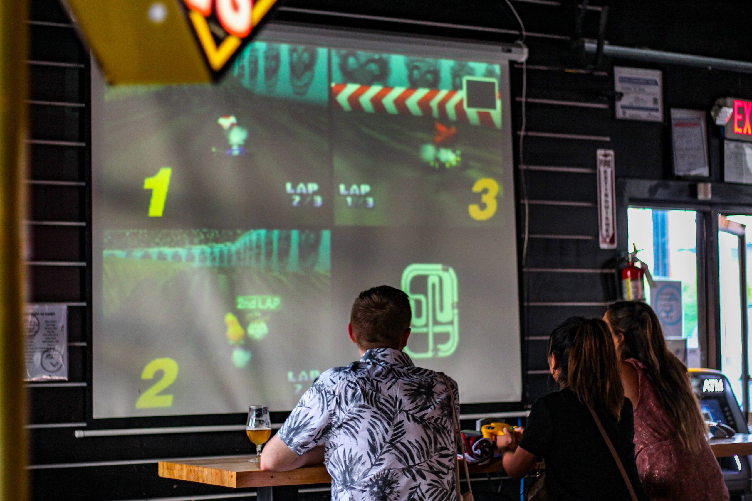 eople sitting at a table, focused on a video game screen displaying colorful graphics and action.