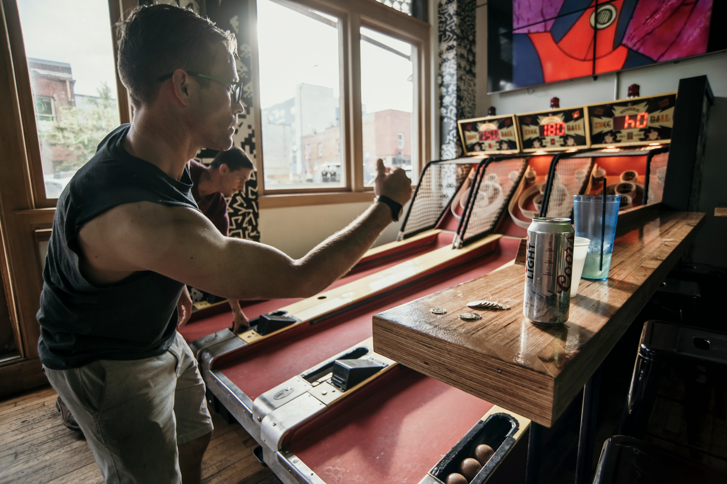 A man engaged in a game of pinball at a bar, with vibrant lights reflecting off the machine and a lively atmosphere.