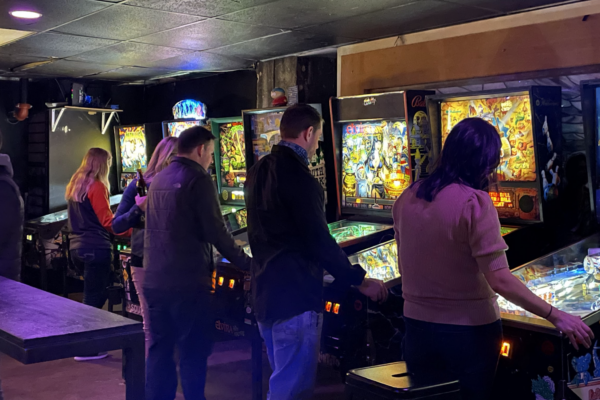 Several individuals engaged in playing pinball machines at a bar, surrounded by vibrant decor and the buzz of conversation. Several individuals engaged in playing pinball machines at a bar, surrounded by vibrant decor and the buzz of conversation.