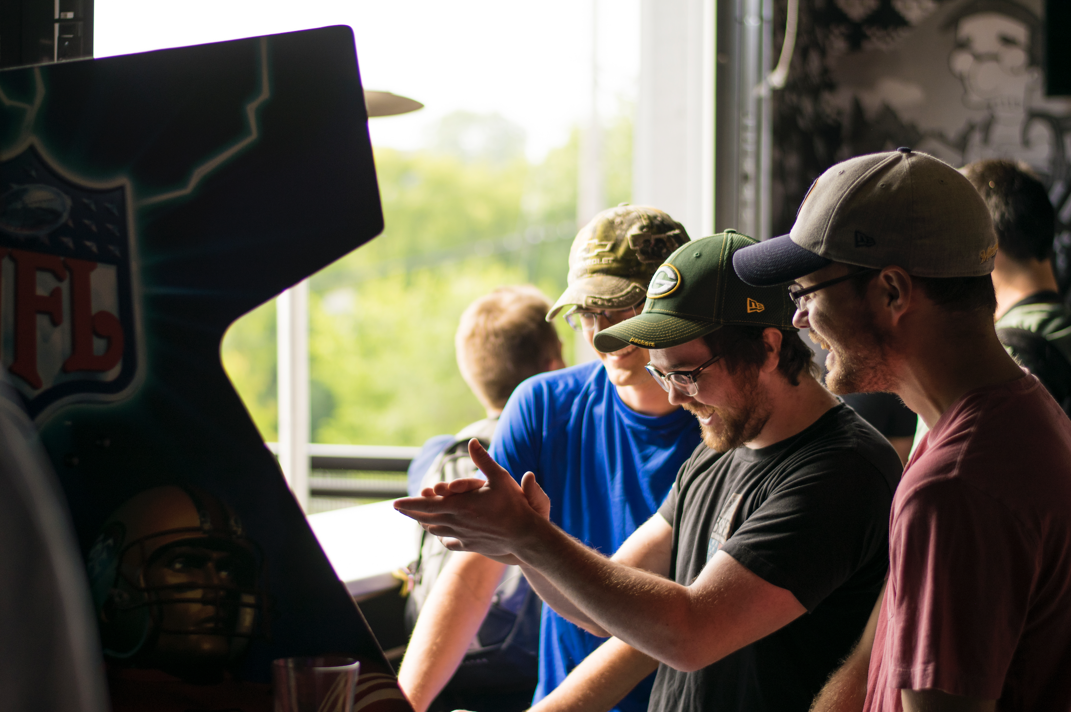 A group of men surrounds a television, focused on the screen as they share reactions and comments about the show