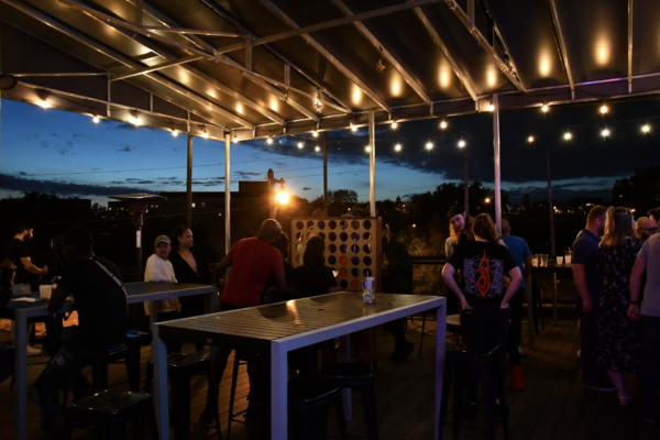 Patrons relaxing at tables under a canopy of string lights on a charming outdoor patio Patrons relaxing at tables under a canopy of string lights on a charming outdoor patio
