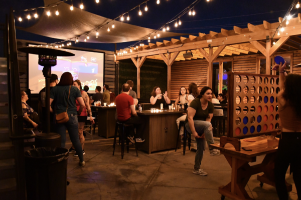 A group of people socializing at tables in a sunny patio area, enjoying their time outdoors A group of people socializing at tables in a sunny patio area, enjoying their time outdoors
