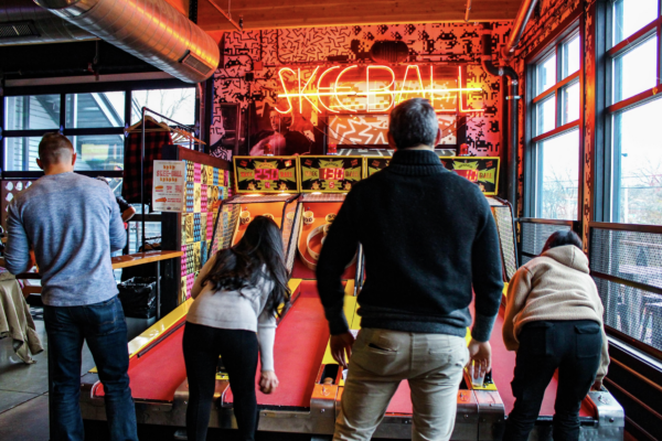 A group of people enjoying a lively game of pinball in a vibrant game room filled with various machines A group of people enjoying a lively game of pinball in a vibrant game room filled with various machines