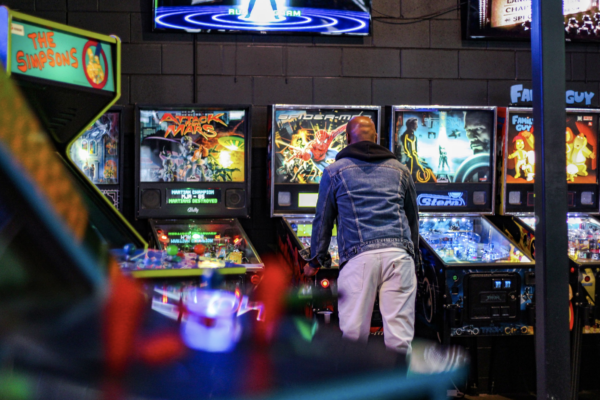 A man focused on playing a pinball machine in a vibrant game room filled with various arcade games A man focused on playing a pinball machine in a vibrant game room filled with various arcade games