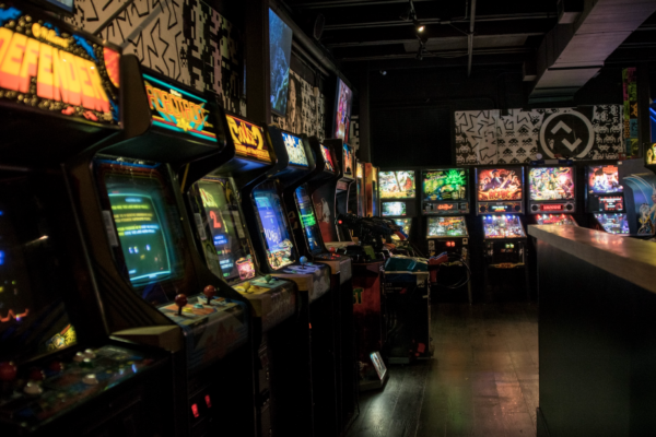 A low-light interior shot of a row of classic arcade games lined up against a wall. A low-light interior shot of a row of classic arcade games lined up against a wall.