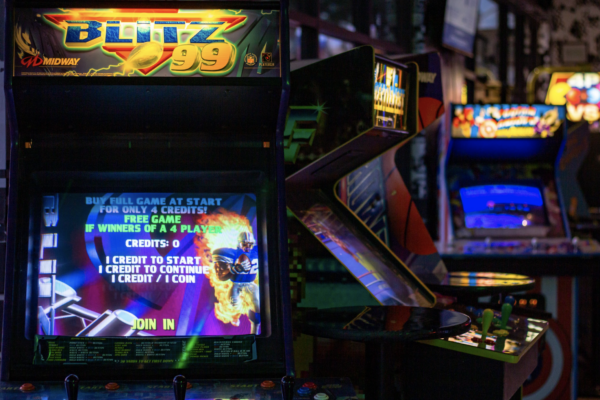 A blurred, close-up shot of several arcade machines with brightly lit screens showing different games. A blurred, close-up shot of several arcade machines with brightly lit screens showing different games.