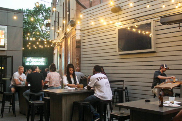 blurry, wide shot of people sitting at tables on a patio decorated with string lights at dusk blurry, wide shot of people sitting at tables on a patio decorated with string lights at dusk