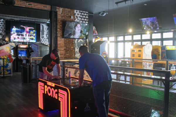 A blurry shot of two men playing an illuminated "PONG" table game in a crowded room. A blurry shot of two men playing an illuminated "PONG" table game in a crowded room.