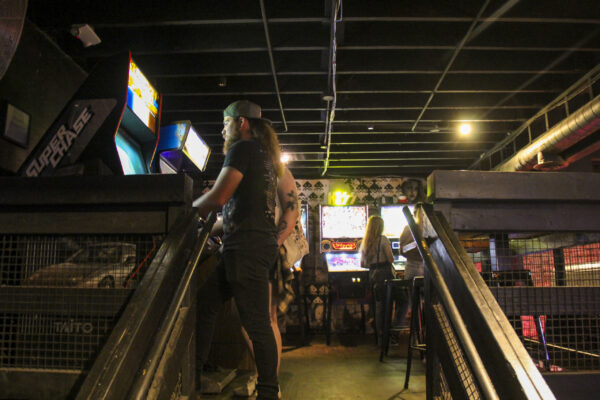 A man stands on a stairway surrounded by colorful arcade machines, enjoying the vibrant gaming atmosphere A man stands on a stairway surrounded by colorful arcade machines, enjoying the vibrant gaming atmosphere