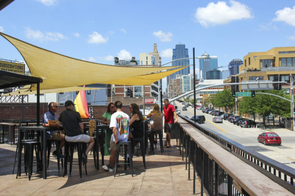 People dining at tables on a patio with a city skyline visible in the background People dining at tables on a patio with a city skyline visible in the background