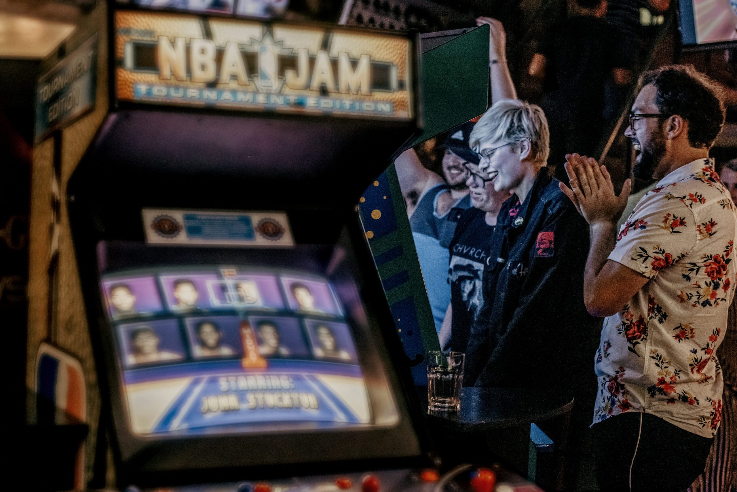 A group of people gathered around a video game machine, engaged and watching the gameplay intently