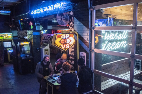 A group of people gathered around a table in front of a bar, engaged in conversation and enjoying their time together A group of people gathered around a table in front of a bar, engaged in conversation and enjoying their time together