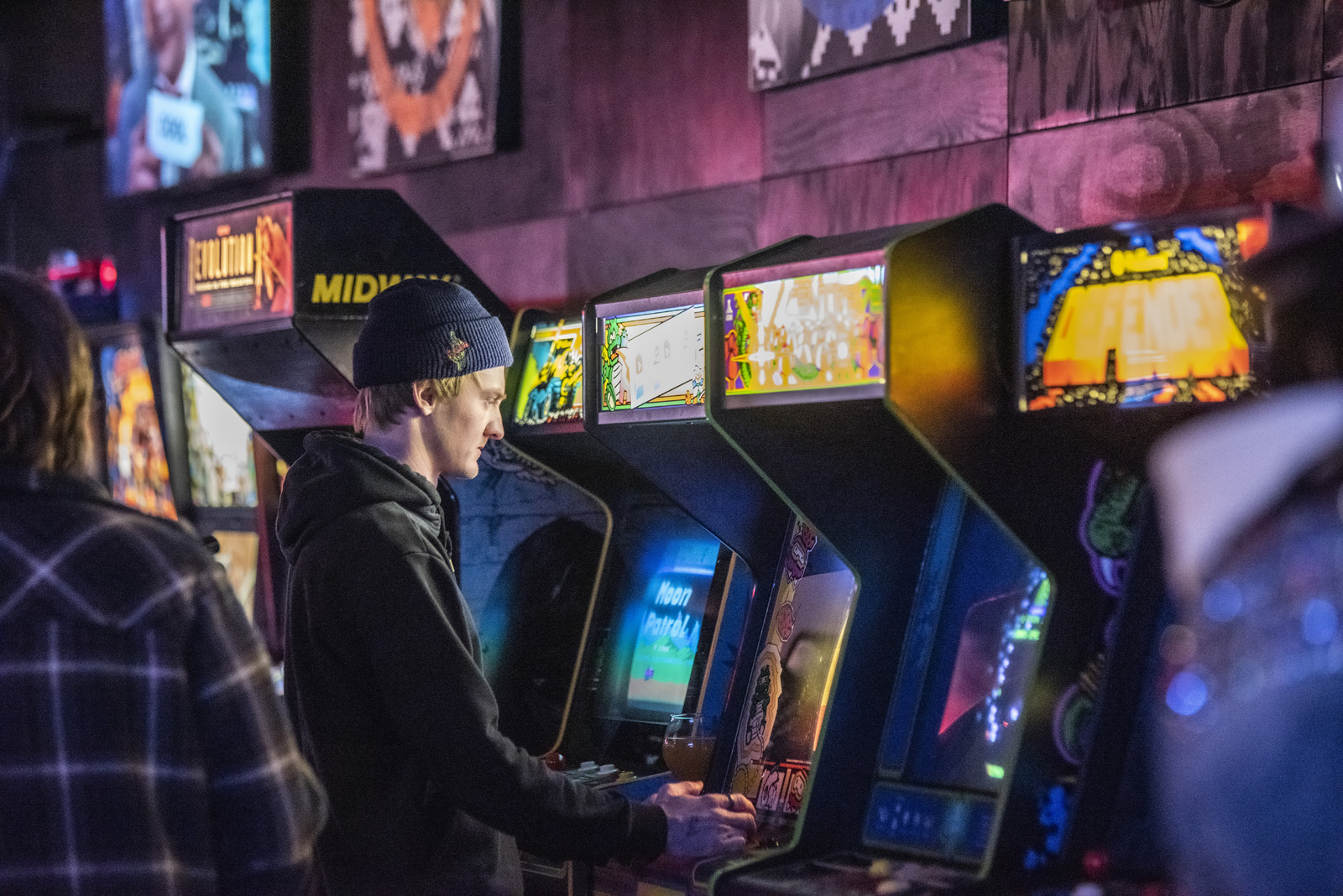 A man focused on playing video games surrounded by colorful arcade machines in a lively gaming room