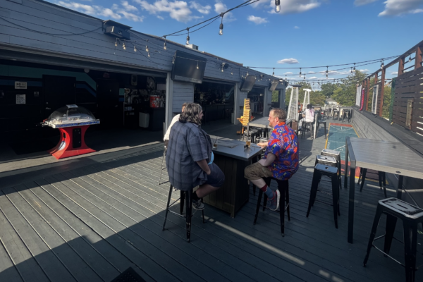Up-Down Arcade Bar Outdoor Patio An outdoor patio at Up-Down Arcade Bar featuring tables, string lights, and metal staircases, with a relaxed atmosphere under a clear blue sky.